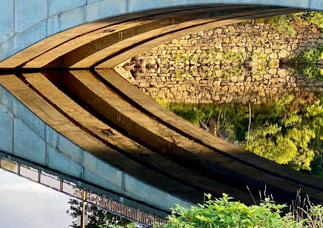 Centennial Bridge in Kingfield. Low evening light reflects the ceiling of the arch in the still water of the Mill Pond in the Carrabassett River.  See our exhibition at Cove Street Arts in Portland, ME #kingfieldmaine #carrabassettriver #orcuttphotography #covestreetarts #historicbridges #mainetheway #downeastmagazine #mainephotofraphy #portlandcameraclub #portlandcameraclubmaine